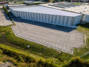 Aerial view of a large industrial warehouse with a spacious parking lot and surrounding green area.
