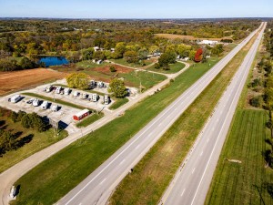 Aerial view of a highway alongside an RV park with several parked vehicles and green fields.