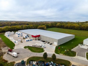 Aerial view of a large warehouse facility with a gray roof and red accents, surrounded by storage containers.