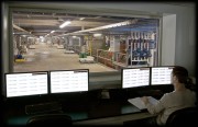 Individual monitoring data on multiple screens in a control room overlooking an industrial facility.