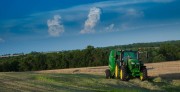 Green tractor working in an agricultural field under a blue sky with clouds.