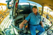 A farmer seated in a tractor cab, operating controls with a focused expression while working in a field.