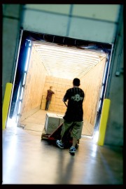 A worker pushing a cart into a brightly lit loading dock with stacked boxes inside.
