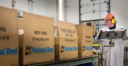Worker in a processing facility wearing a hard hat and ear protection while handling boxes labeled \'National Beef\'.