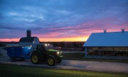 Tractor pulling a blue feed mixer in front of a barn during sunset.