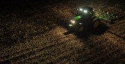 Tractor equipped with lights working in a field during nighttime.