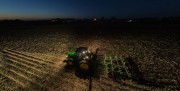 A tractor equipped with a plow working in a field illuminated by its headlights during nighttime.