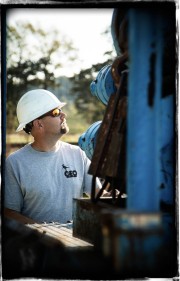 Man wearing a hard hat and sunglasses looking up at industrial equipment in a construction setting.