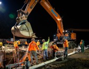 Construction workers operating heavy machinery at a nighttime excavation site.