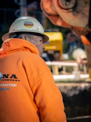 Construction worker wearing an orange hoodie and hard hat, observing a construction site.