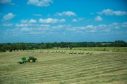 Green tractor working in a field with round hay bales scattered across the landscape.