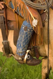 Close-up of a cowboy boot with decorative stitching and a saddle on a horse.