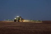 Tractor equipped with a sprayer working in an agricultural field during nighttime with lights illuminated.