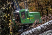 Green forestry machine working in a wooded area with fallen trees and autumn foliage.