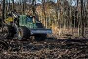 A green forestry machine with large tires working in a wooded area with trees in the background.