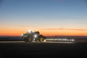 John Deere tractor equipped with lights plowing a field during sunset.