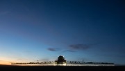 Agricultural sprayer operating in a field during dusk with a clear sky and faint light.