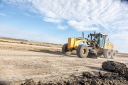 Yellow grader machine leveling dirt on a construction site under a clear sky.