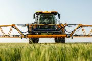 Agricultural sprayer tractor with extended arms in a green field of crops.