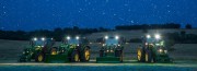Four tractors lined up in a field at night with lights on and stars in the sky.