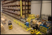 Interior view of a warehouse showing forklifts and stacked pallets on shelves.