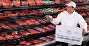 A grocery store employee holding a can while standing in front of a meat display case filled with various beef products.