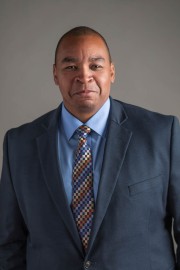 Man wearing a blue suit and patterned tie, posing for a professional portrait.