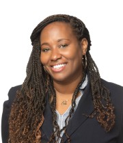 Woman with braided hair wearing a dark blazer and smiling at the camera.