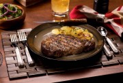 Grilled ribeye steak served on a plate with potatoes and a side salad.