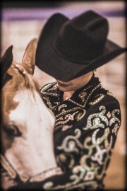 Individual wearing a black cowboy hat and a sequined jacket, standing next to a horse with a white face.