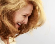 Woman with long, flowing blonde hair smiling with her head tilted downwards.