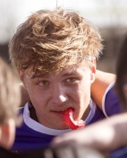 Young male rugby player with a red mouthguard and tousled hair looking at the camera.