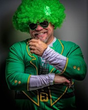 Man wearing a green curly wig, sunglasses, and a green St Patty\'s Day costume with a plaid design, smiling at the camera.
