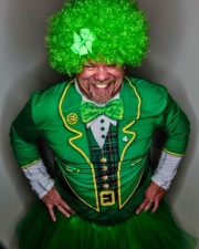 Man wearing a green costume with a curly green wig and bowtie, smiling at the camera.