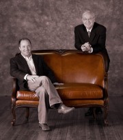 Two men seated and standing on a brown leather couch in a studio setting.