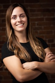 Woman with long hair and a black shirt smiling while standing with arms crossed.