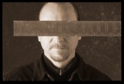 A man with a ruler placed horizontally across his face, obscuring his eyes and forehead.