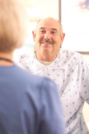 A male patient wearing a hospital gown smiling while talking to a healthcare professional.