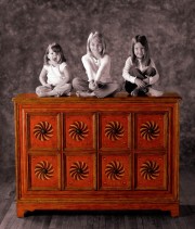Three children sitting on top of a wooden chest with decorative carvings.