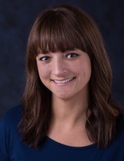 Headshot of a woman with brown hair and a blue shirt, smiling at the camera.
