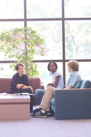 Three individuals engaged in a discussion while seated in a student union area with large windows.