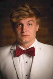 Young man wearing a white suit and a red striped bow tie, looking directly at the camera.