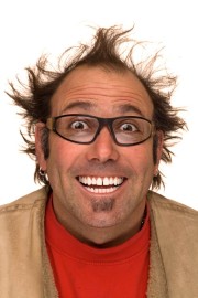 A man with spiky hair and glasses smiling widely, wearing a red shirt and beige jacket.