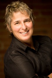 A smiling individual with short, light-colored hair wearing a black shirt in a headshot.