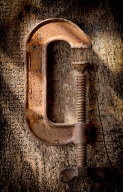 Rusty C-clamp positioned on a wooden surface with visible wear and tear.