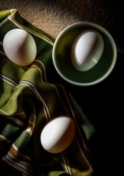 Three white eggs, two on a green cloth and one in a green bowl, arranged in a top-down view.