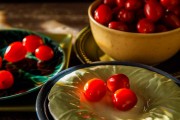 Several cherry tomatoes placed on different colored plates with a bowl of tomatoes in the background.