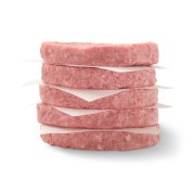 Five raw ground beef patties stacked with parchment paper in between each patty.