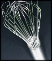 Close-up of a stainless steel whisk with a long handle and multiple wire loops.