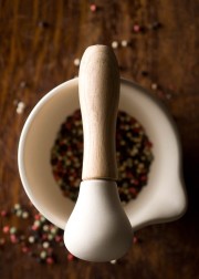 White mortar and pestle with a wooden handle, filled with mixed peppercorns.